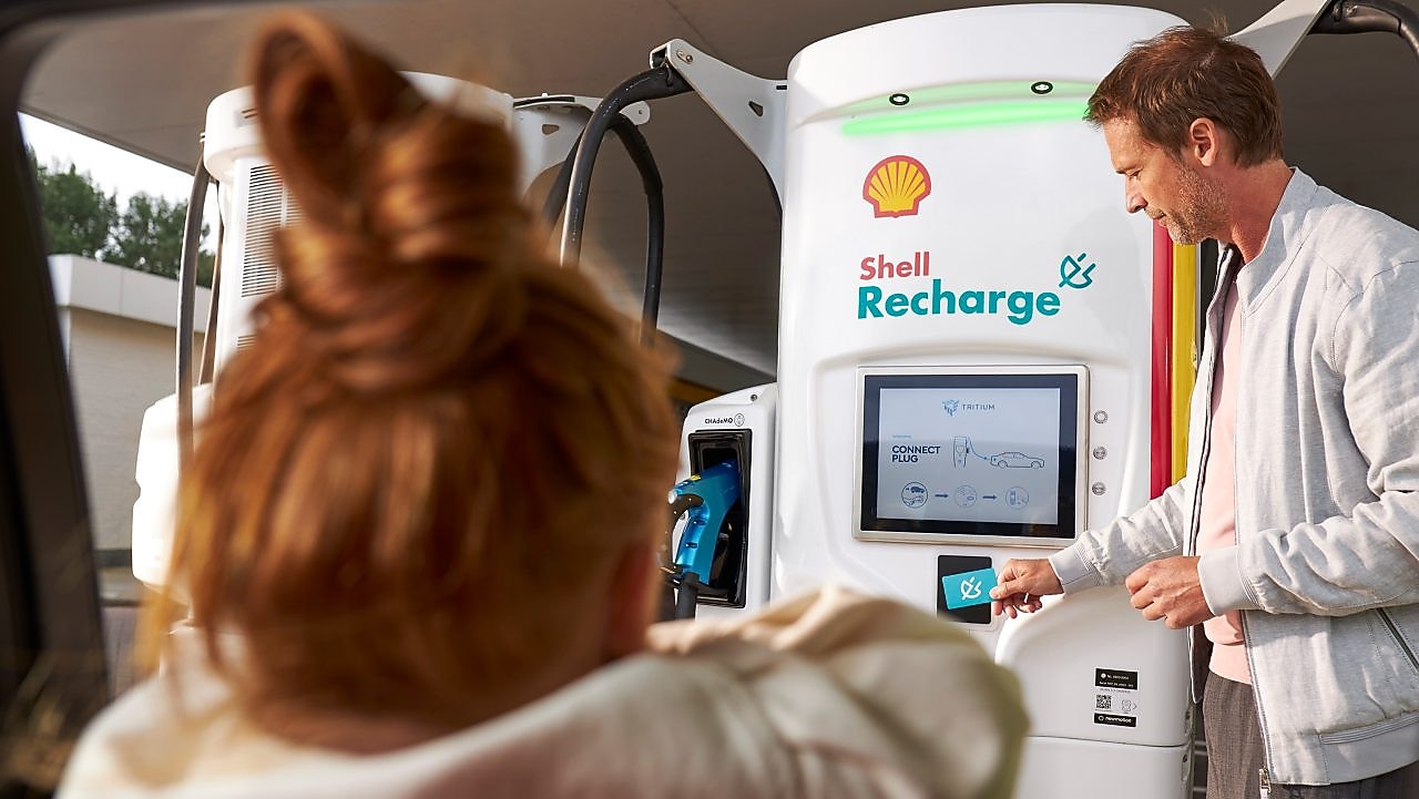 A man using a Shell Recharge unit while a girl watches from inside a car