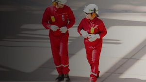 Male and female worker in red overalls and white helmets and hearing protection walking