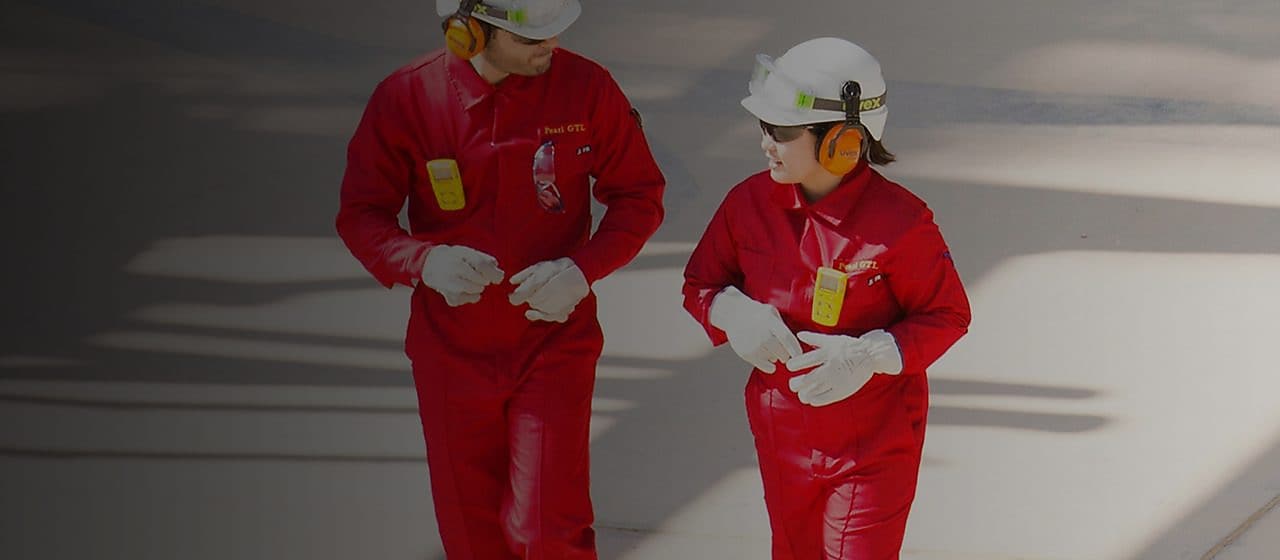Male and female worker in red overalls and white helmets and hearing protection walking