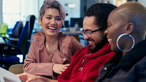 Three people in an office sitting together, looking at papers and laughing
