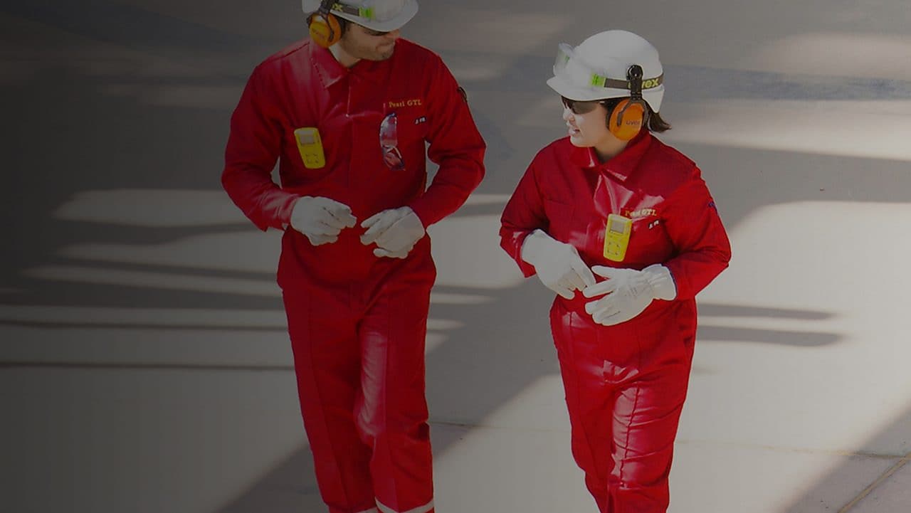 Male and female worker in red overalls and white helmets and hearing protection walking