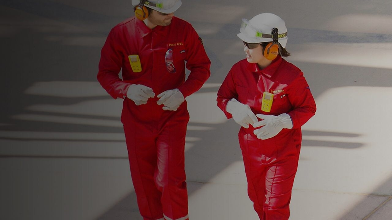Male and female worker in red overalls and white helmets and hearing protection walking