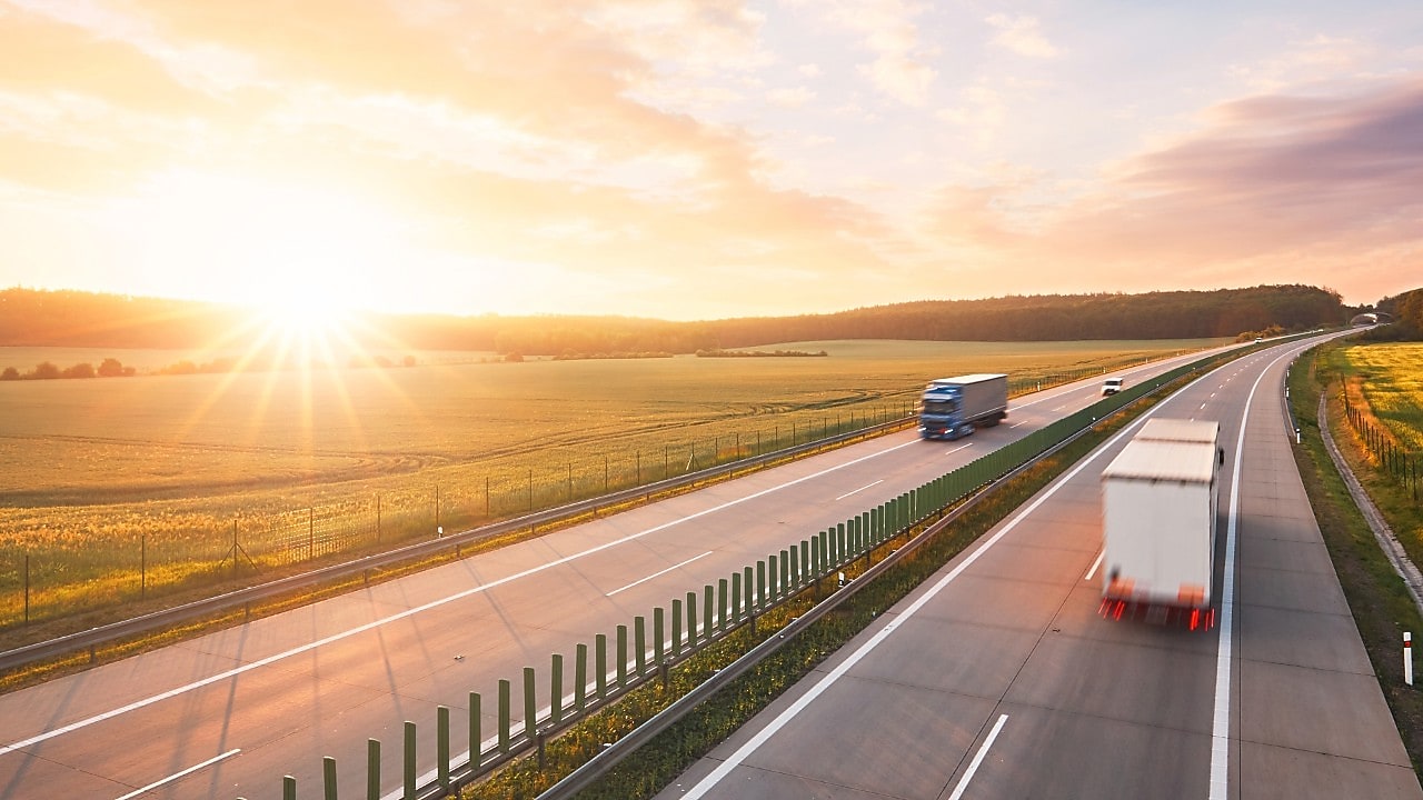 Trucks driving on a highway at sunset.