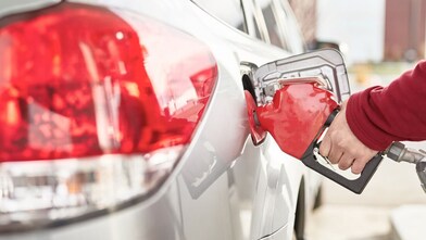 A man's hand holding a fuel nozzle while pumping gas into the car.
