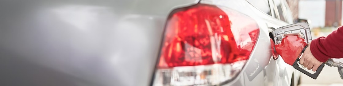 A man's hand holding a fuel nozzle while pumping gas into the car.