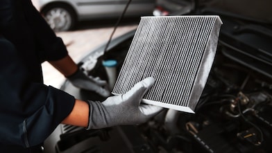 Mechanic holding an air filter next to a car engine.