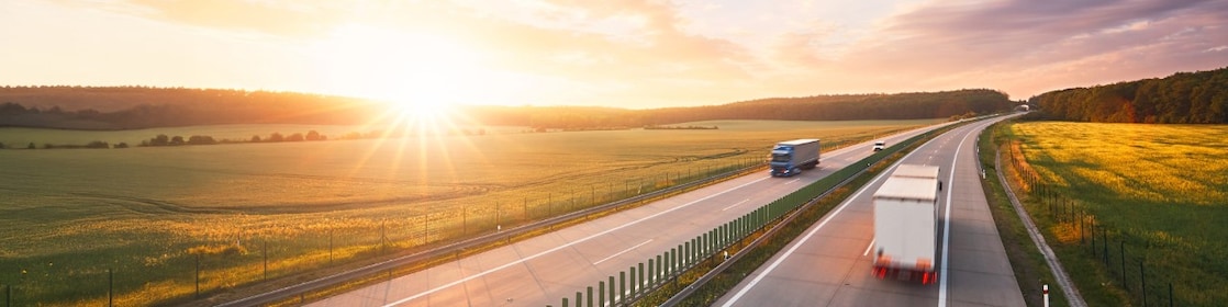 Trucks driving on a highway at sunset.