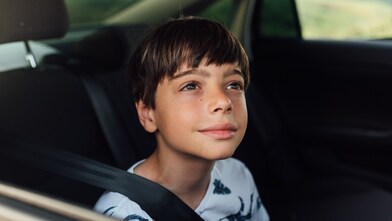 Boy wearing a seatbelt, sitting in the back seat of a car, looking out the window.