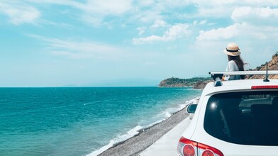 Woman standing beside her car appreciating ocean view