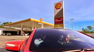 Red car with two people in front of a Shell gas station.