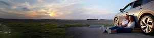 Couple sitting next to a car at sunset.