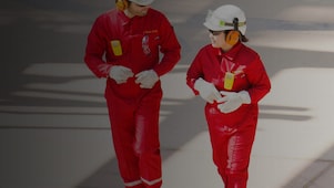 Trabajador y trabajadora con overoles rojos, cascos blancos y protección auditiva caminando