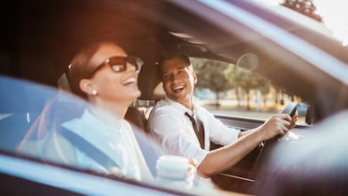 Pareja compuesta por hombre y mujer sentada en los asientos delanteros de un auto.