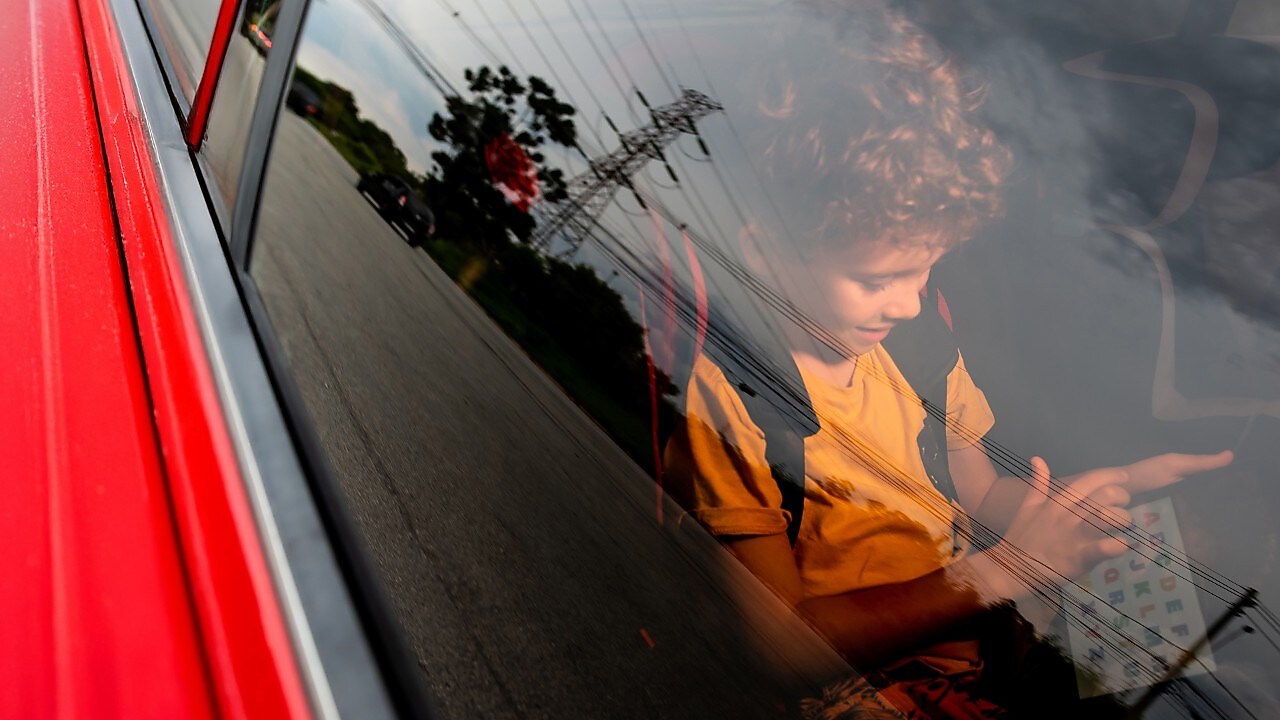 Niño mirando una tablet dentro de un auto rojo.
