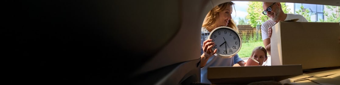 Familia descargando cajas y un reloj del baúl de un auto.