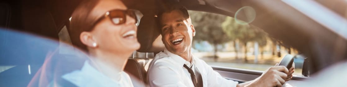 Pareja compuesta por hombre y mujer sentada en los asientos delanteros de un auto.