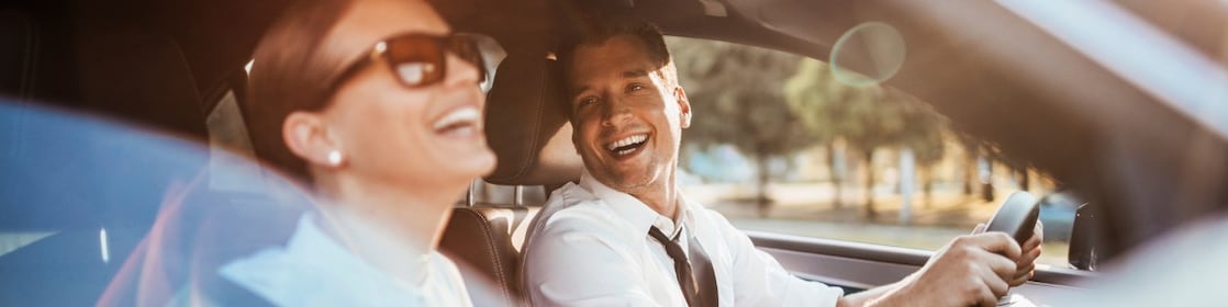 Pareja compuesta por hombre y mujer sentada en los asientos delanteros de un auto.