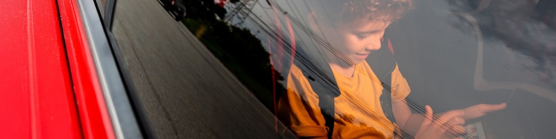 Niño mirando una tablet dentro de un auto rojo.