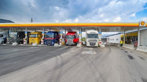 Gasolinera Shell con seis camiones aparcados. De izquierda a derecha: un camión blanco, verde oscuro, amarillo, azul oscuro, rojo y otro camión blanco.